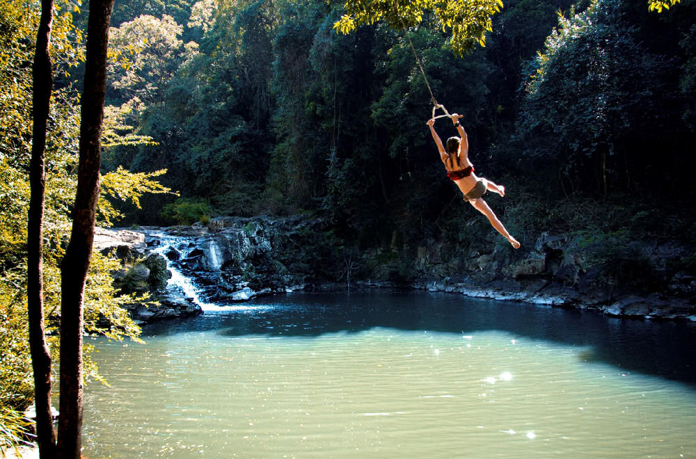 a woman swinging on a tree swing into a creek