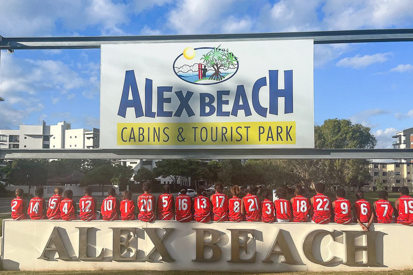 Sporting group under the entrance sign to Alex Beach Cabins and Tourist Park Sunshine coast